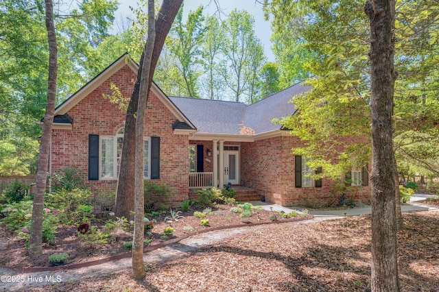 view of front facade featuring roof with shingles, covered porch, and brick siding
