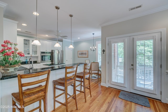 kitchen featuring white cabinets, glass insert cabinets, visible vents, stainless steel appliances, and a peninsula