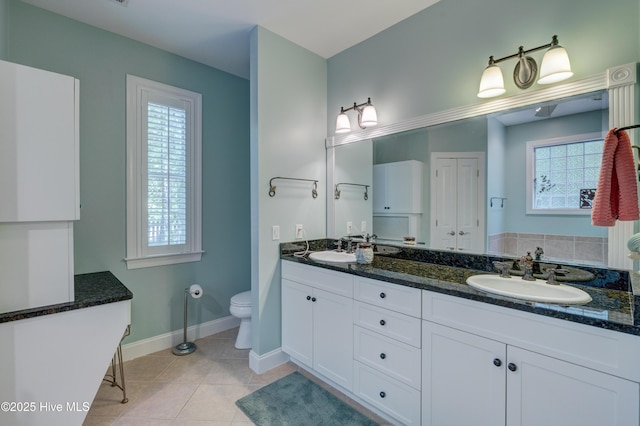 bathroom featuring a sink, toilet, double vanity, baseboards, and tile patterned flooring