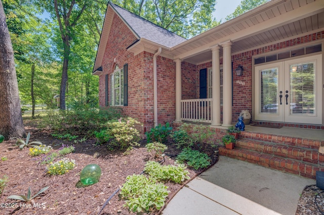 view of front of property featuring covered porch, brick siding, french doors, and a shingled roof