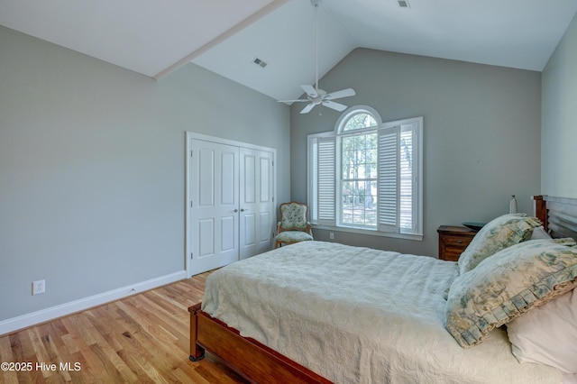 bedroom with wood finished floors, a closet, baseboards, visible vents, and high vaulted ceiling