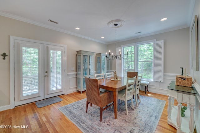 dining area featuring a notable chandelier, light wood-type flooring, crown molding, visible vents, and wainscoting