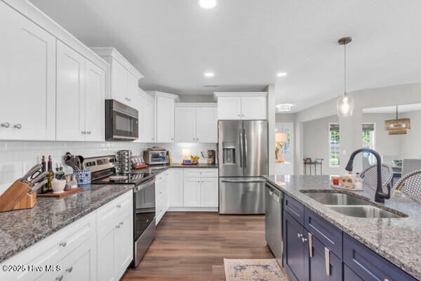 kitchen with decorative light fixtures, appliances with stainless steel finishes, a sink, white cabinetry, and dark wood-type flooring