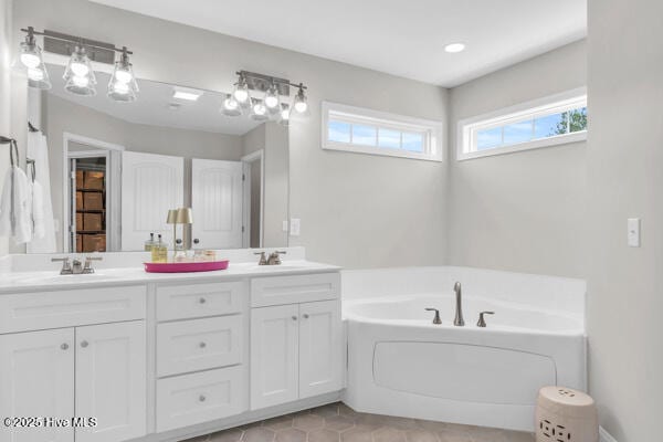 full bathroom with double vanity, a bath, tile patterned flooring, and a sink