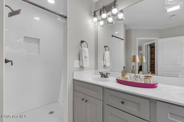 full bath featuring a tile shower, double vanity, and a sink