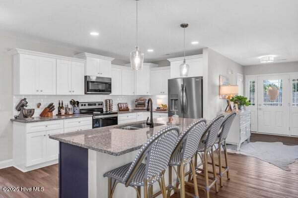 kitchen with dark wood finished floors, dark stone countertops, appliances with stainless steel finishes, and decorative backsplash