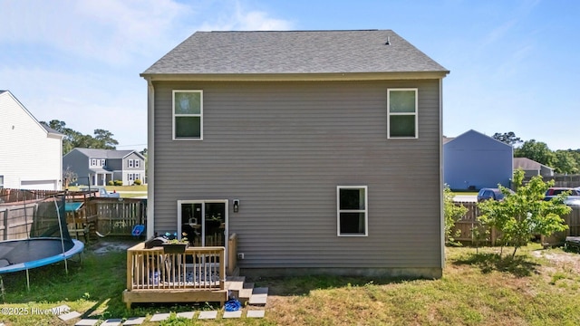 rear view of property with a trampoline, a yard, a wooden deck, and a fenced backyard