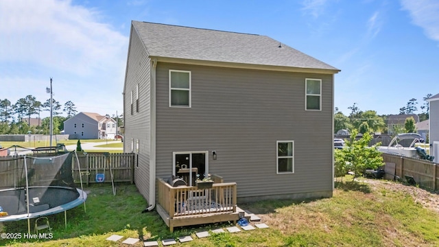 rear view of property featuring a trampoline, a wooden deck, fence private yard, and a lawn