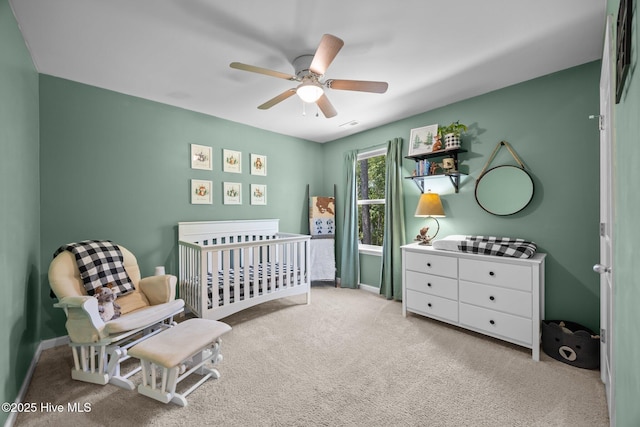 carpeted bedroom with ceiling fan, baseboards, and a crib