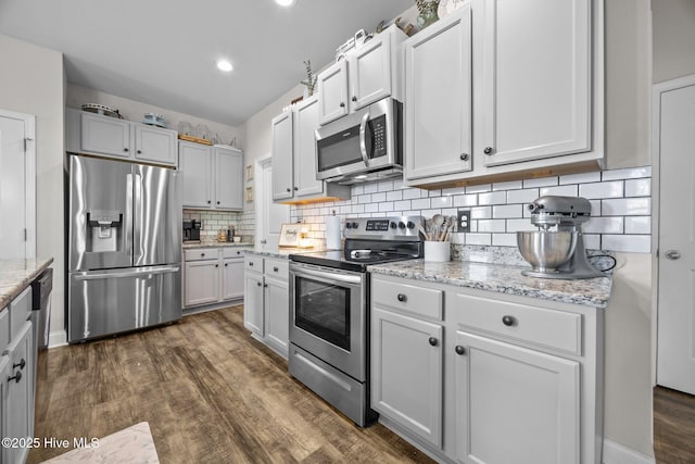 kitchen featuring appliances with stainless steel finishes, light stone counters, dark wood-style flooring, and backsplash