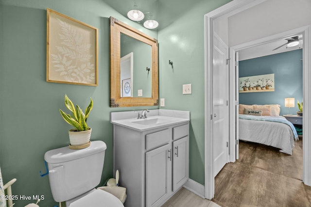 ensuite bathroom with toilet, ensuite bathroom, wood finished floors, vanity, and baseboards