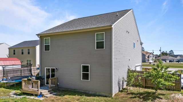 back of house with a trampoline, a residential view, a shingled roof, and fence