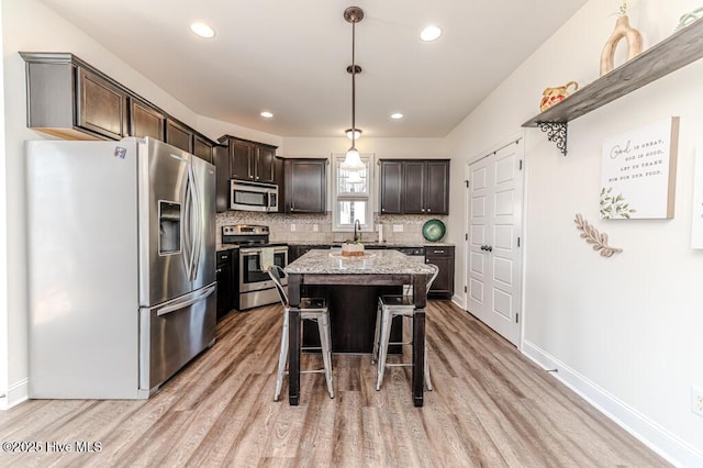 kitchen with backsplash, a kitchen bar, appliances with stainless steel finishes, light wood-type flooring, and dark brown cabinets