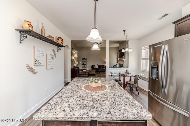 kitchen with dark brown cabinetry, visible vents, light wood-type flooring, light stone counters, and stainless steel fridge