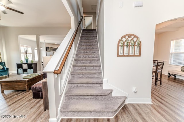 staircase with arched walkways, baseboards, a ceiling fan, and wood finished floors