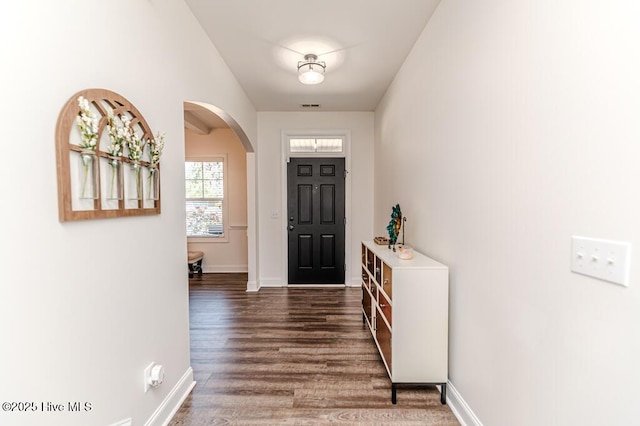 foyer with arched walkways, baseboards, visible vents, and dark wood-type flooring