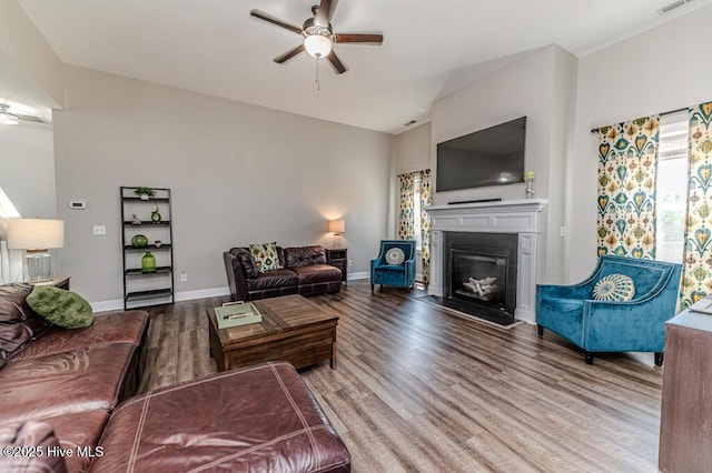 living area with baseboards, ceiling fan, a glass covered fireplace, and wood finished floors