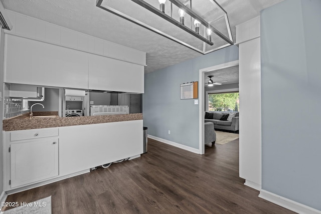 kitchen featuring dark wood-style flooring, washer / dryer, baseboards, white cabinetry, and a sink