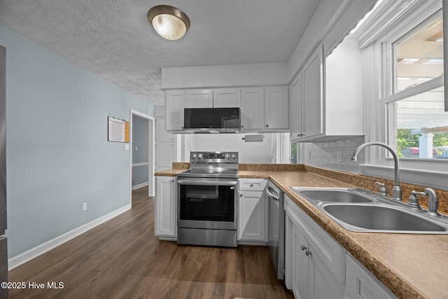 kitchen with dark wood-style flooring, appliances with stainless steel finishes, a sink, white cabinetry, and baseboards