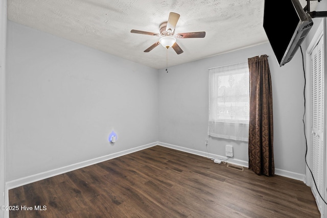empty room with a ceiling fan, a textured ceiling, visible vents, dark wood finished floors, and baseboards