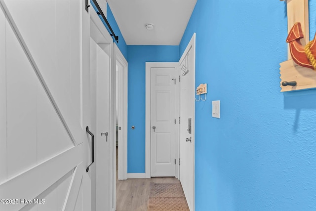 hallway featuring baseboards, a barn door, and light wood-style floors