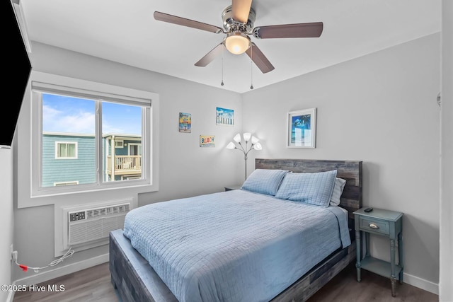 bedroom with a ceiling fan, baseboards, wood finished floors, and a wall mounted air conditioner