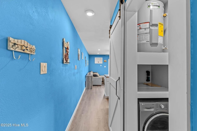 hallway featuring washer / clothes dryer, baseboards, a barn door, and light wood finished floors