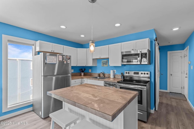kitchen with a sink, stainless steel appliances, light wood-type flooring, and white cabinetry