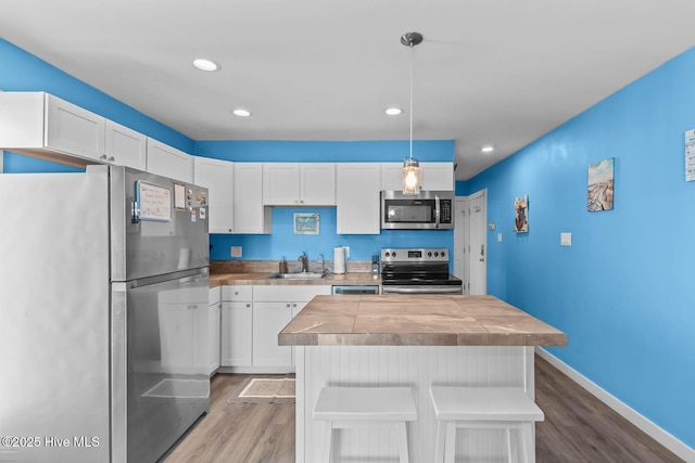 kitchen with a sink, light wood finished floors, appliances with stainless steel finishes, and white cabinetry