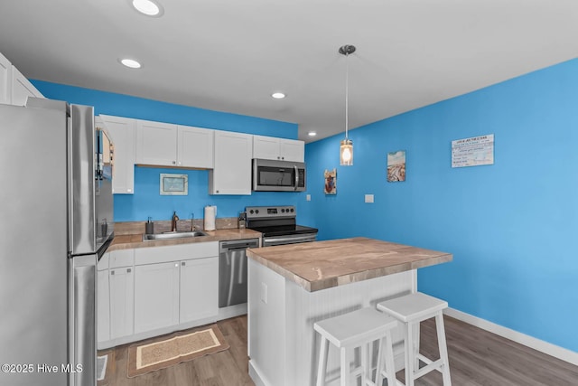 kitchen with a kitchen bar, a sink, white cabinets, stainless steel appliances, and light wood-style flooring
