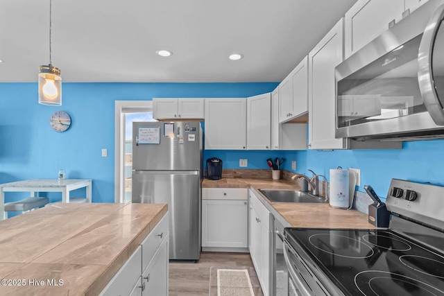 kitchen with stainless steel appliances, white cabinetry, a sink, and light wood-type flooring