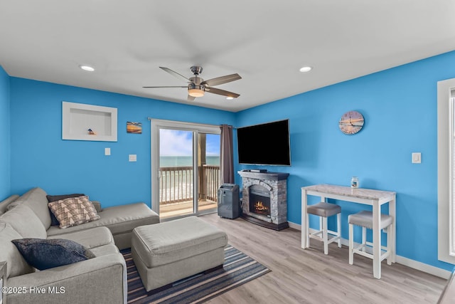 living room featuring wood finished floors, ceiling fan, baseboards, and a fireplace