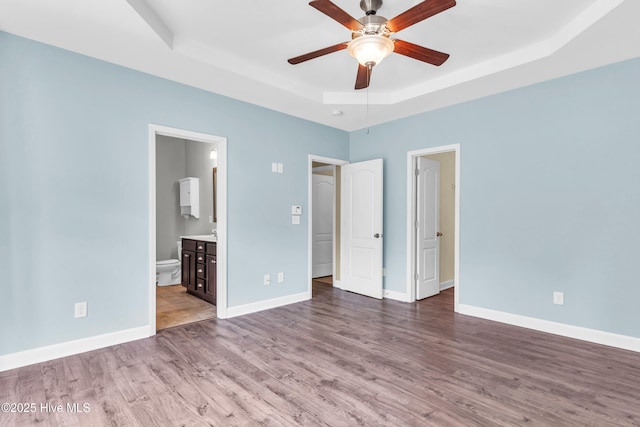 unfurnished bedroom with a raised ceiling, wood finished floors, baseboards, and ensuite bathroom
