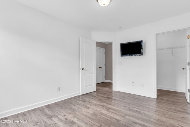 unfurnished bedroom with wood finished floors, a walk in closet, baseboards, and a closet
