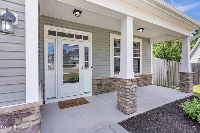 entrance to property with stone siding, covered porch, and fence