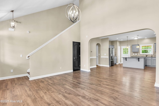 unfurnished living room with arched walkways, wood finished floors, baseboards, and a towering ceiling