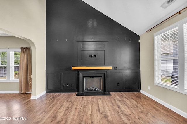 unfurnished living room with high vaulted ceiling, a fireplace with flush hearth, wood finished floors, baseboards, and arched walkways