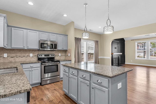 kitchen featuring appliances with stainless steel finishes, gray cabinets, a center island, backsplash, and healthy amount of natural light