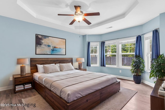 bedroom with a tray ceiling, baseboards, and wood finished floors