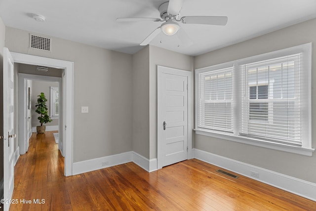 unfurnished bedroom with wood-type flooring, a ceiling fan, baseboards, and visible vents