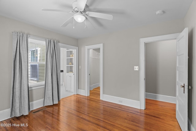 unfurnished bedroom with visible vents, wood finished floors, baseboards, a closet, and a spacious closet