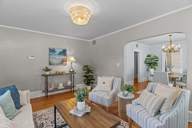 living area featuring visible vents, ornamental molding, wood finished floors, arched walkways, and a notable chandelier
