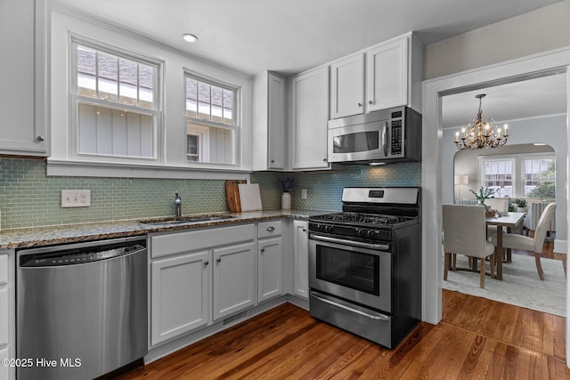 kitchen featuring light stone countertops, appliances with stainless steel finishes, a sink, a chandelier, and dark wood finished floors