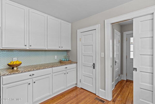 kitchen with white cabinets, backsplash, visible vents, and light wood-style floors