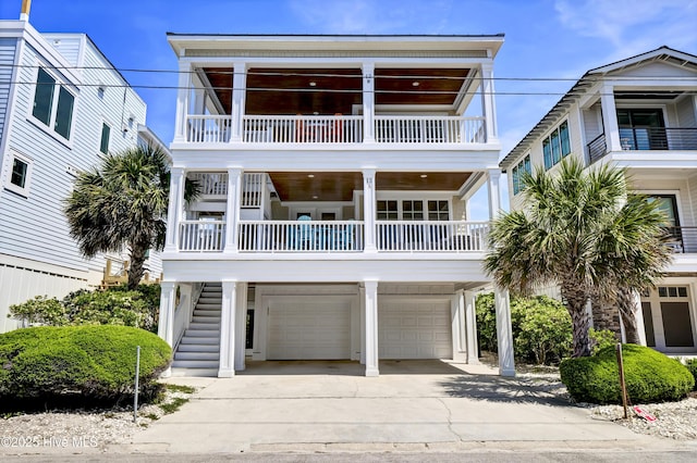 coastal inspired home with a garage, concrete driveway, stairway, and a balcony