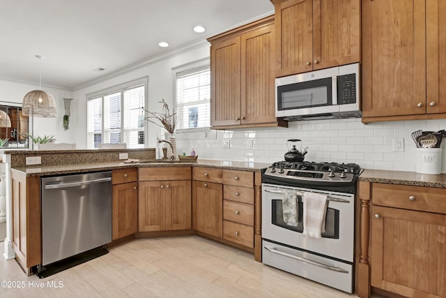 kitchen featuring brown cabinets, appliances with stainless steel finishes, dark stone countertops, a peninsula, and ornamental molding
