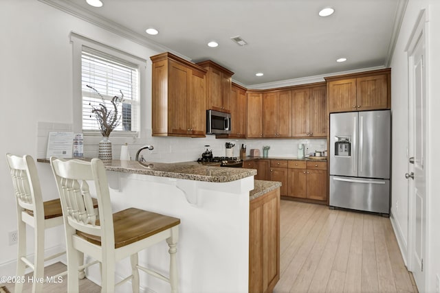 kitchen with backsplash, appliances with stainless steel finishes, brown cabinets, a peninsula, and dark stone counters
