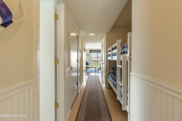 corridor with wainscoting, wood finished floors, and a decorative wall