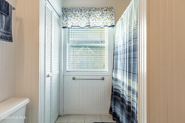 bathroom with tile patterned floors, toilet, a shower with curtain, and wood walls