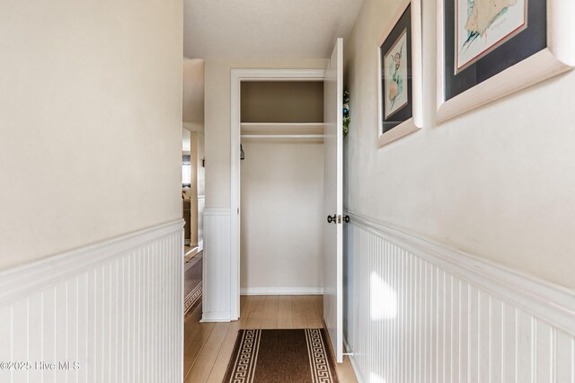 hall featuring wood finished floors, a decorative wall, and wainscoting
